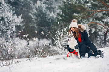 Cute girl in a winter park. Woman palying with a dog. Lady in a black jacket