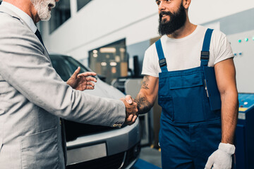 Obraz premium Car mechanic talking with senior business man costumer during periodic car condition check. Technical inspection.