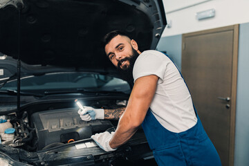 Car mechanic working at vehicle maintenance garage. He is doing periodic car condition check.