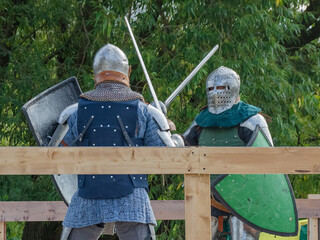 Two foot warriors in heavy medieval armor fight in the arena. Armed with swords. They are protected...