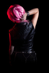 Back view of stylish pink haired young rocker woman in leather vest.