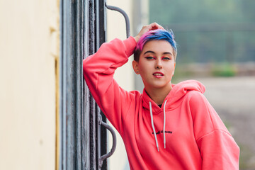 Portrait of a young girl with short colorful hair and nose piercing satanding near the wall with...