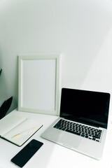 White room working space with blank screen laptop, book, smartphone.