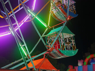 A ferris wheel, decorated with colorful lights, at a local temple fair in Thailand during the night