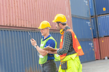Engineer man in hardhat and safety vest talks on two-way radio, foreman worker holding clipboard checklist at containers cargo, Teamwork concept