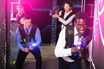 Cheerful smiling men and women in business suits playing laser tag emotionally in dark room