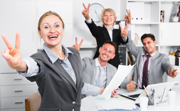 Happy team with businesswoman on foreground emotionally gesturing and celebrating victory at office