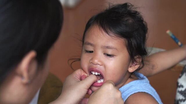 Mother cleaning her daughter's teeth with Dental floss indoor.