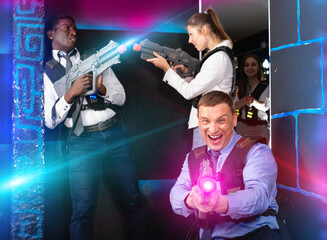 Happy smiling men and women in business suits playing laser tag emotionally in dark room