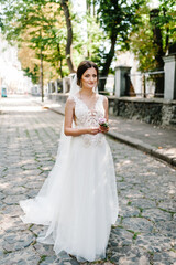 Beautiful bride in white dress is waiting for the groom in the park.