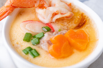 Homemade style steamed egg with shrimp and vegetables in a ceramic bowl on wooden table. healthy food concept.