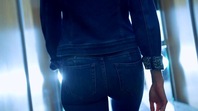 camera shoots female model wearing jeans and denim jacket walking from behind. denim model. indoor.
