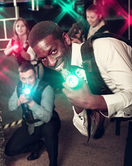 Positive men and women in business suits playing laser tag emotionally in dark room