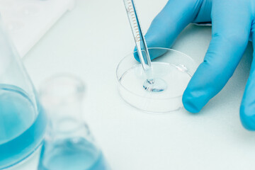 Close up of process of pipetting blue liquid from a flask into a Petri dish.Concept of chemical technology, biotechnology, pharmaceuticals.Selective focus with shallow depth of field, copy space
