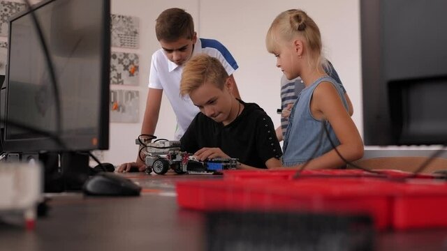 Group of kids building robot constructor from the plastics details programmed on the computer, at robotics school lesson.