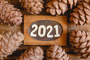 Wooden sign with the date 2021 on a wooden background. There are fir cones around the numbers. Top...