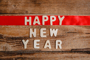 Happy new year inscription in wooden letters on a wooden background. The word happy on the red ribbon. Flat lay.