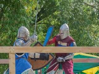 Two foot warriors in heavy medieval armor fight in the arena. Armed with swords. They are protected...