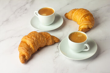 cup of strong coffee and fresh croissant close-up on white background.