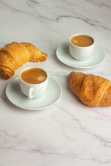 two white cups with black coffee and croissants on a white background.