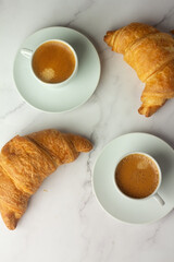 two white cups with black coffee and croissants.