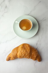 a cup of black strong coffee and a fresh croissant.