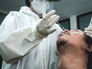 An unidentifiable nurse start to insert a long q-tip into a patient's nose for a nasopharyngeal...