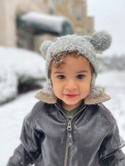 Cute Moroccan toddler walking while snowing  in city with funny expression