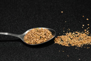 Coriander powder in steel spoon and on black background 