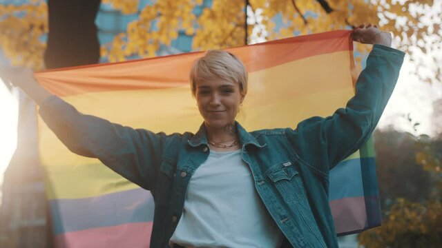 beutiful young woman with short blond hair spinning the rainbow flag around herself in the park in autumn. High quality 4k footage