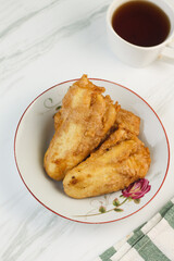 Pisang Goreng or Banana fritters, Indonesian traditional snack made from banana and flour, deep fried. Served on white plate, with a cup of tea. Isolated white background. Copy space for text. 