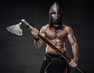 Strong and furious nord barbarian posing in dark studio background holding his two handed axe on...