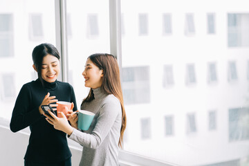 Two Asian business women were chatting by the window during recess
