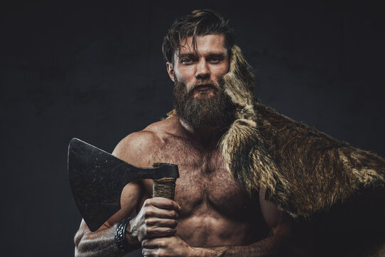 Medieval scandinavian warrior with muscular naked build posing with his hunting trophy and axe in dark studio background.