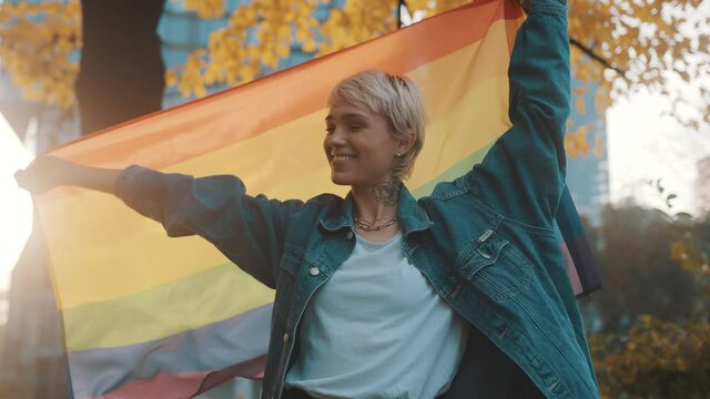 beutiful young woman with short hair waving rainbow flag in the park. High quality 4k footage
