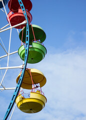 Multi-colored cabins of the Ferris wheel against the blue sky.