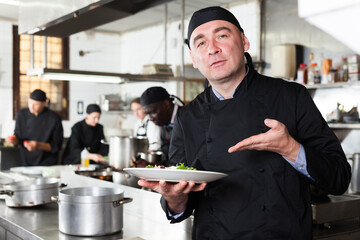 Positive male cook with cooked dish in restaurant kitchen. High quality photo