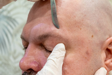 Fototapeta premium a female cosmetologist plucks a man's eyebrows with tweezers