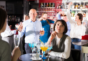 Bored adult woman sitting at table, having no fun at corporate party in bar