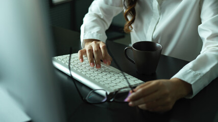 Female hand holding eyeglasses and typing on computer keyboard