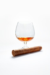 Closed up view of glass of cognac with cigar aside on white back