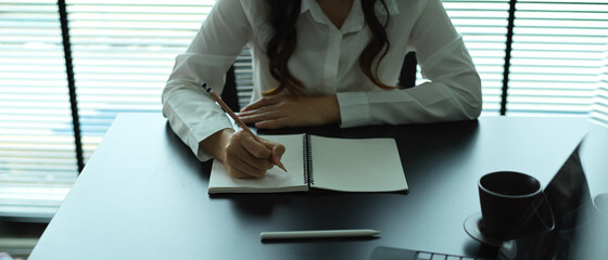 Female office worker writing on blank notebook on meeting table