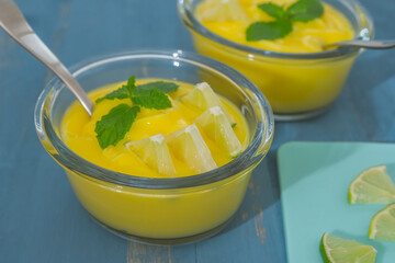 Lemon pudding or lemon curd  in glass bowls served with mint leaves and sliced lemon close up on blue wooden background, sweet cream, delicious dessert