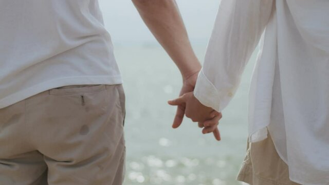 Close up couple hold hands while standing on the beach on holiday summer, asian loving couple holding hands on a beach near the sea.