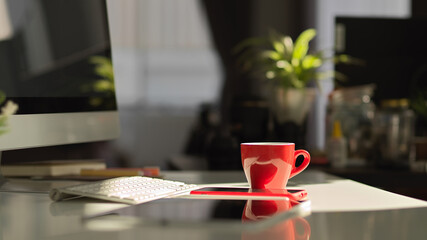 Red coffee cup on worktable with smartphone, tablet, computer and supplies
