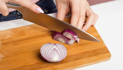 a woman cuts Red onions with a knife on a cutting Board