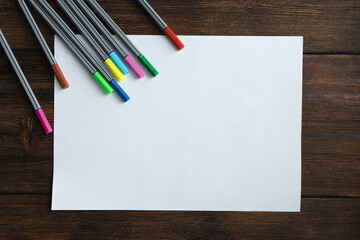 Blank, white sheet of paper with colored markers on dark wooden background
