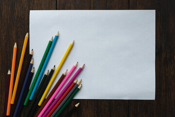 Blank, white sheet of paper with colored pencils on dark wooden background