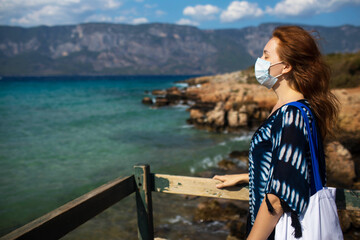 Beautiful woman travels during quarantine in a mask by the sea and beach.