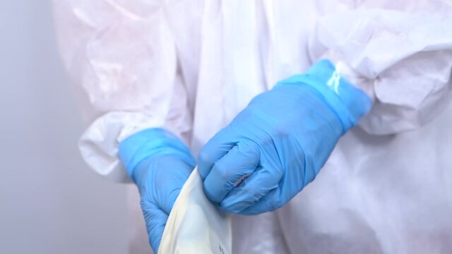 Nurse in protective PPE suit putting on gloves to work